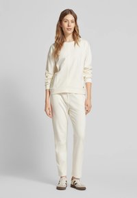 Felpa color crema e pantaloni jogger realizzati in tessuto morbido, con un design semplice e polsini a costine, abbinati a sneaker coordinati.