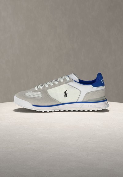 Λευκό και γκρι αθλητικό παπούτσι με μπλε λεπτομέρειες, σχέδιο με κορδόνια, υφασμένα πάνελ και λογότυπο Polo στο πλάι και τη φτέρνα, τοποθετημένο σε ανοιχτή επιφάνεια.