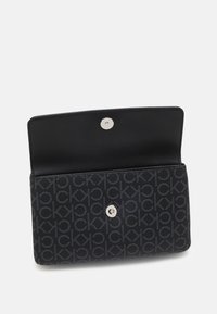 Černá peněženka vyrobená z texturovaného materiálu s opakujícím se vzorem loga. Má zavírání na patent a vnitřek bez viditelných přihrádek.