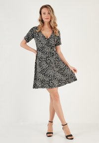 Black and white leopard print dress with a wrap design, short sleeves, and a fitted waist, made of lightweight fabric. Black heeled sandals.