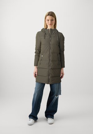 Doudoune vert olive, longueur genoux, avec capuche, motif matelassé, fermeture éclair à l'avant et deux poches zippées. Portée sur un jean déchiré.