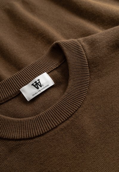 Pull en tricot brun avec un col ras du cou côtelé et une étiquette en tissu portant le nom de la marque. Fini texturé avec une apparence douce.