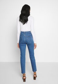 Vysoké modré džíny se zúženým střihem, se zadními kapsami a jemnými švy. Nosit s úzkým bílým topem s dlouhým rukávem a podpatky.