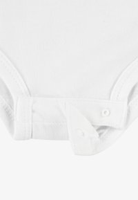 Body din bumbac alb cu închideri cu capse în partea de jos, având o textură netedă și deschideri elastice pentru picioare pentru confort și ușurință în utilizare.