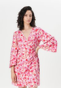 Abito avvolgente floreale con motivi in stile acquerello rosa e rosso, scollatura a V, maniche a campana 3/4 e dettaglio con fiocco laterale. Tessuto morbido.