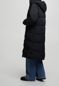 Czarna kurtka puchowa z kapturem i zapięciem na zamek, z pikowanym wzorem i bocznymi kieszeniami, w połączeniu z szerokimi niebieskimi dżinsami i czarnymi botkami.