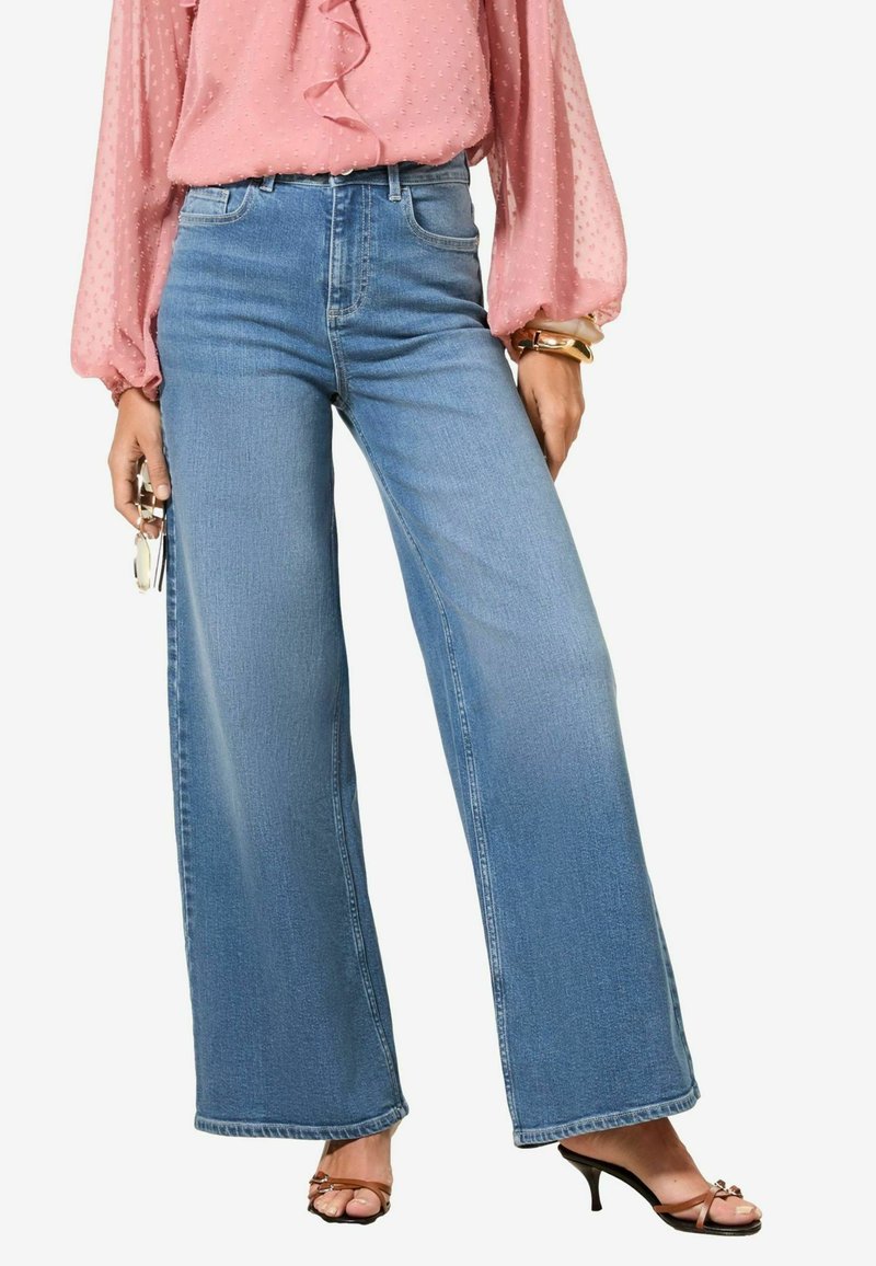 Široke modre denim hlače z visokim pasom in gladko površino, v kombinaciji z roza bluzo in čevlji z visoko peto.