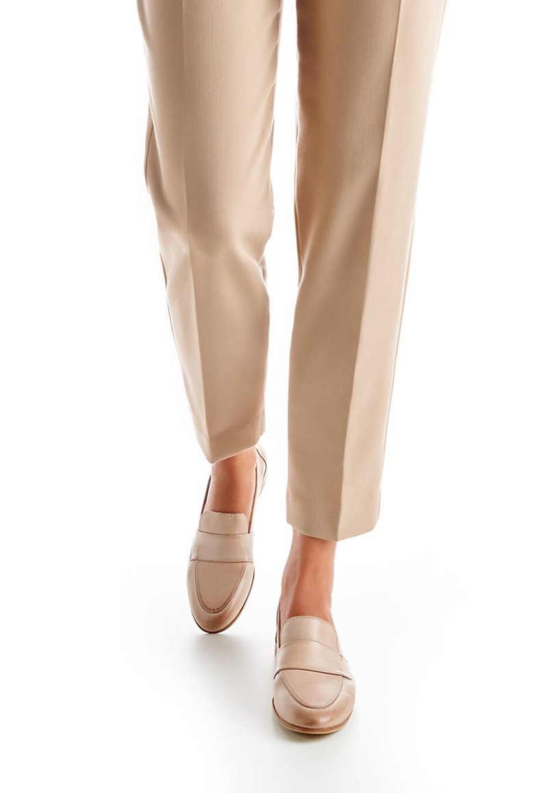 Beige leren loafers met een gladde afwerking en een gestikte detail over het wreefdeel. Gecombineerd met lichtbeige, op maat gemaakte broek.