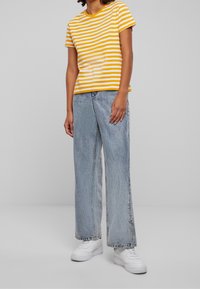 Yellow and white striped short-sleeve t-shirt paired with light blue wide-leg jeans and white sneakers. Simple design with a casual style.