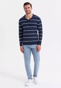 Polo tričko s dlouhým rukávem v námořnické modré barvě s pruhy, s límečkem a žebrovaným lemem, kombinované se světle modrými džíny a bílými teniskami.