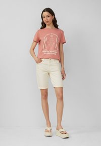 Różowa bawełniana koszulka z białym nadrukiem graficznym, w połączeniu z kremowymi szortami dżinsowymi podwiniętymi na końcach oraz jasnymi klapkami na platformie.