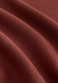 Rostfärgad tyg med en slät, strukturerad yta och subtila räffelmönster, som visar mjuka veck och draperingar.