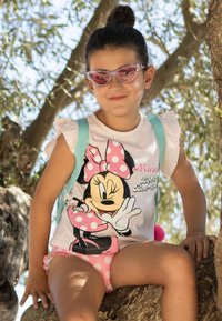 Maglietta bianca senza maniche a tema Minnie Mouse con maniche arricciate, dettagli rosa e pantaloni a pois, abbinati a occhiali da sole rosa e uno zaino azzurro chiaro.