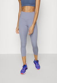 Jasnoszare legginsy o średnim stanie z eleganckim fasonem, zestawione z niebieskimi i fioletowymi butami sportowymi z teksturowaną cholewką i akcentami.