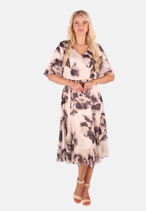 Blumenkleid in sanftem Beige mit großen grauen und lila Mustern, V-Ausschnitt, ausladenden Ärmeln und einem fließenden A-Linien-Rock, kombiniert mit nude-farbenen Absätzen.