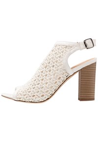 Bílé sandály s otevřenou špičkou na vysokém podpatku, s tkanou svrchní částí a nastavitelným páskem kolem kotníku. Obsahují texturovaný blokový podpatek a hladké okraje.