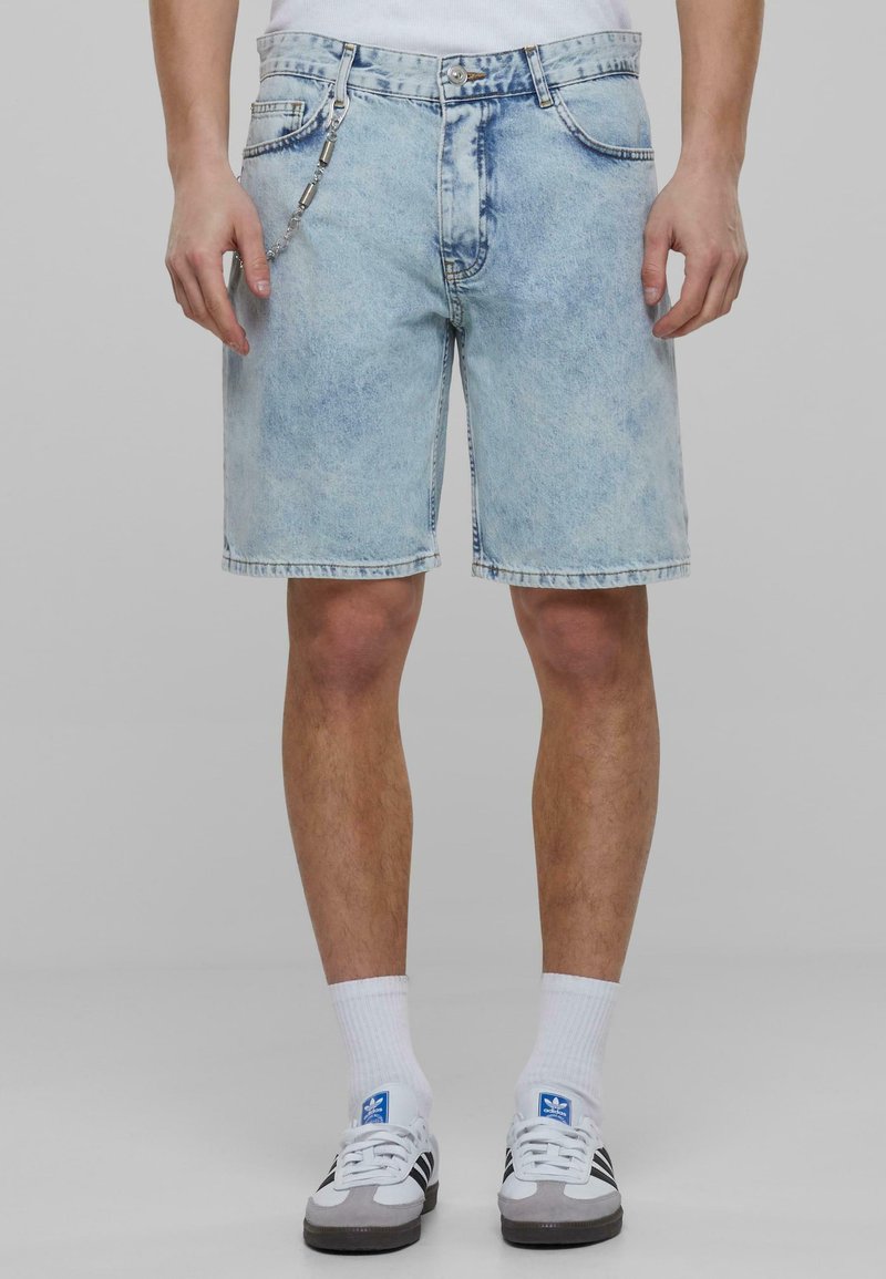 Shorts de mezclilla azul claro con un lavado descolorido, cinco bolsillos y un detalle de cadena plateada en la parte frontal. Corte recto con un dobladillo a la altura de la rodilla.
