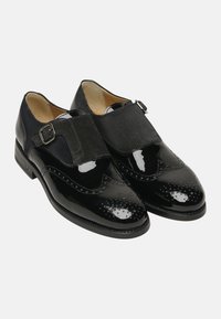 Schwarze Lacklederschuhe mit Wildlederakzenten und dekorativen Perforationen, ausgestattet mit einer abgerundeten Zehe und einer seitlichen Schnalle zum Verschließen.