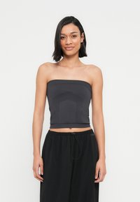 Haut noir sans bretelles en matière extensible avec un détail texturé au centre. Associé à un pantalon noir ample avec un cordon de serrage ajustable.