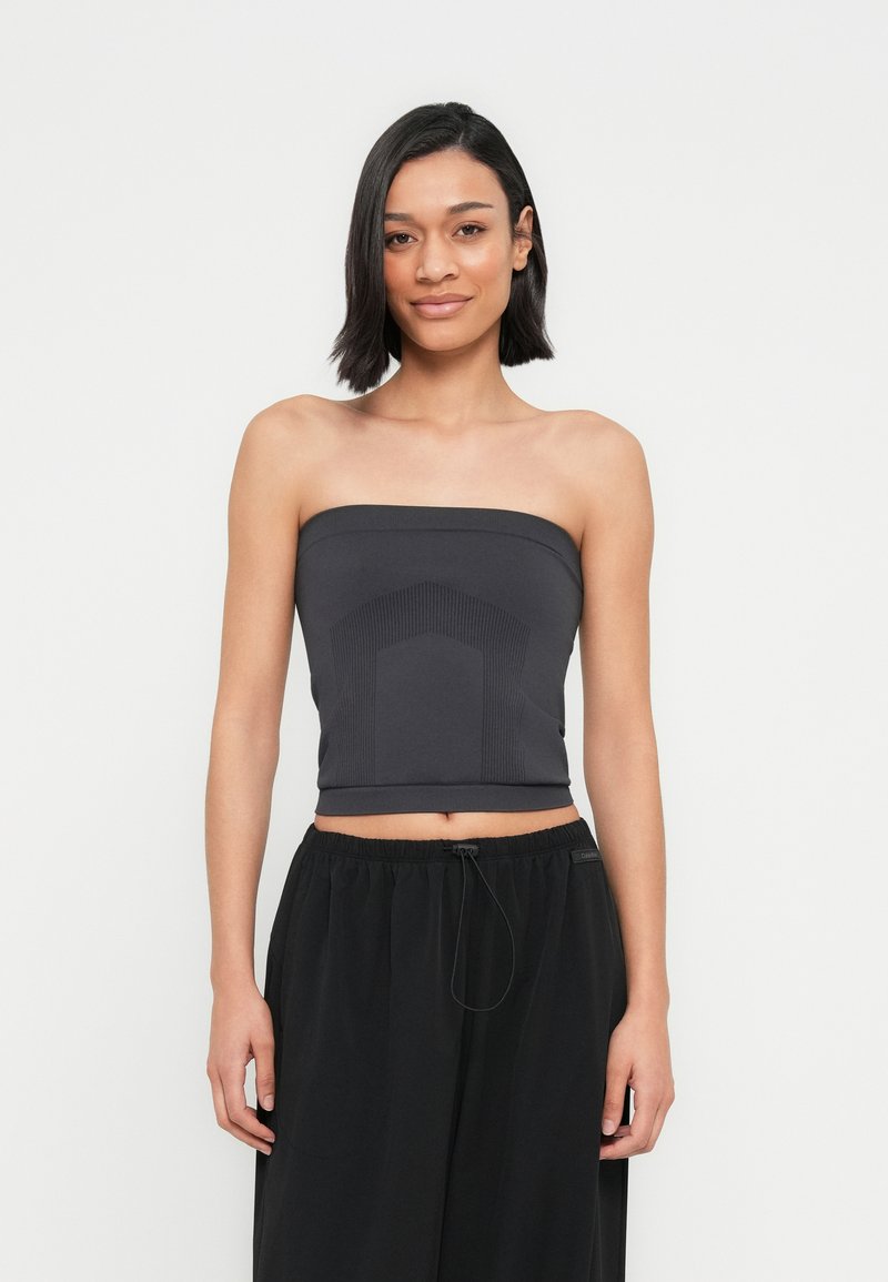 Haut noir sans bretelles en matière extensible avec un détail texturé au centre. Associé à un pantalon noir ample avec un cordon de serrage ajustable.