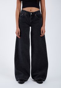 Wide-leg black jeans made of denim with a high waist, five-pocket design, copper hardware, and clean hem finishing at the ankles.