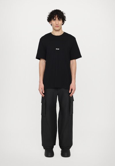 Black t-shirt with a small white logo, paired with loose black cargo pants featuring side pockets and a textured fabric.