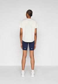 Ανοιχτό γκρι κοντομάνικο πουκάμισο, σκούρα μπλε σορτς με λευκές λεπτομέρειες, συνδυασμένα με λευκά αθλητικά παπούτσια. Απλός σχεδιασμός, λεία υφή και εφαρμοστή γραμμή.