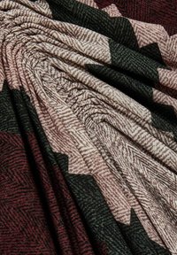 Tkanina s teksturom koja prikazuje cik-cak uzorak u maroon, zelenoj i bež nijansi, s mekanim, naboranim pregibima koji stvaraju dubinu i dimenziju.