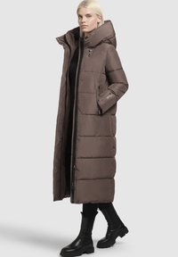 Rjava dolga puffer jakna z visokim ovratnikom, zadrgo in stranskima žepoma. Ima prešito zasnovo in je izdelana iz sijočega materiala.