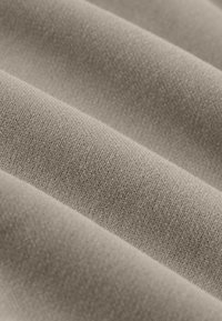 Tissu brun clair à la texture lisse, présentant des motifs en maille fine et un éclat subtil, plié en douces ondulations.