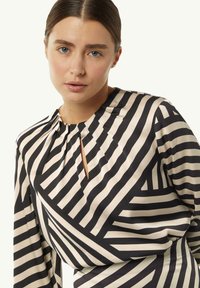 Satinbluse mit schwarzen und cremefarbenen diagonalen Streifen, Schlüsselloch-Ausschnitt und gefälteltem Detail am Kragen, das eine strukturierte Passform bietet.
