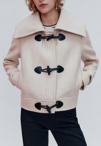 Beżowa kurtka z wełny z dużym kołnierzem, zapięciem na toggle i bocznymi kieszeniami. Charakteryzuje się dopasowanym krojem i teksturowaną tkaniną.