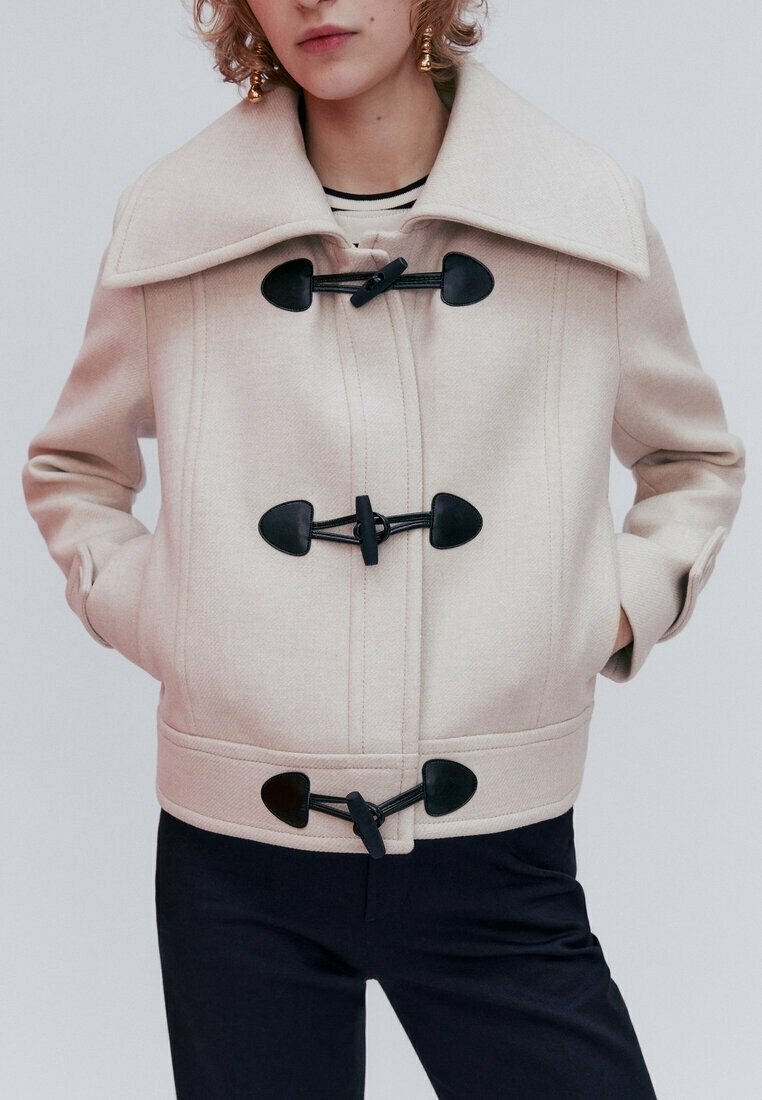 Beżowa kurtka z wełny z dużym kołnierzem, zapięciem na toggle i bocznymi kieszeniami. Charakteryzuje się dopasowanym krojem i teksturowaną tkaniną.