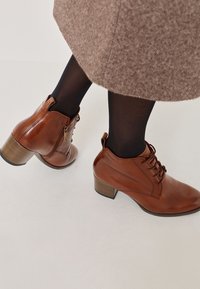 Bottines en cuir marron avec une finition texturée, un design à lacets et un talon bloc de hauteur intermédiaire. Zip à l'arrière pour un enfilage facile.