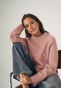 Hea roosa kudumissant sweater kõrge kaelusega ja ribidega mansettidega, koos kergete hallide laiale jalale mõeldud teksadega. Sile tekstuur, juhuslik lõige.