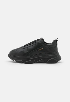Sort lavtop sneaker med tyk geometrisk sål, sorte snørebånd og lille guld "CPNHGN" tekst på siden, vist på hvid baggrund.