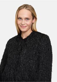 Schwarze, flauschige Jacke mit einer strukturierten, zotteligen Oberfläche, verziert mit metallischen Fadenakzenten für zusätzlichen Glanz. Runder Halsausschnitt und lange Ärmel.