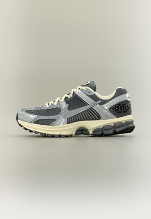 Szaro-czarny but do biegania Nike z kremowymi sznurowadłami i podeszwą, pokazany z boku na jednolitym neutralnym tle.