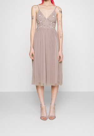 Beige midi dress with a V-neckline, embellished bodice, and a flowing tulle skirt. Silver strappy high-heeled sandals complete the look.