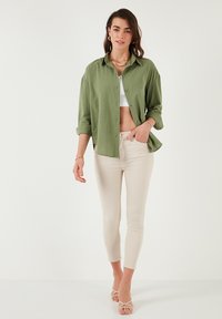 Light green button-up shirt, white crop top, beige fitted pants, and strappy sandals. The shirt has rolled sleeves and a relaxed fit.