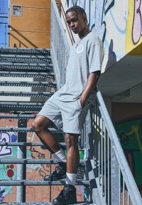 Conjunto de camiseta gris y pantalones cortos, hecho de algodón. Persona de pie en las escaleras, usando zapatillas negras y calcetines blancos, graffiti de fondo.
