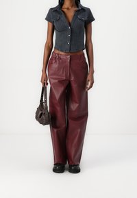 Korte mouwen denim shirt van donkerdenim, met knopen, gecombineerd met wijde bordeaux leren broek. Zwarte robuuste schoenen en een bruine tas.