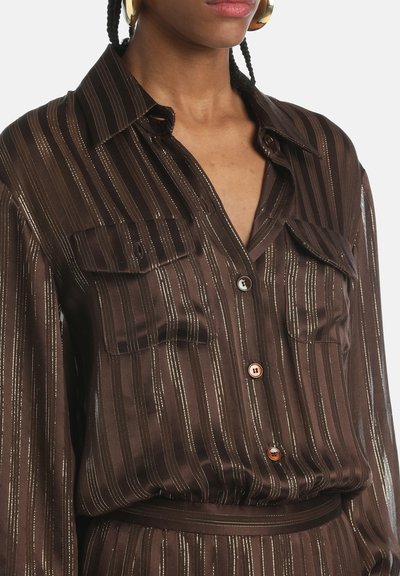 Camisa marrón de botones con sutiles rayas metálicas, dos bolsillos en el pecho, un cuello y una textura suave con cintura ajustable.