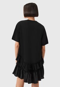 Zwarte jurk met korte mouwen en een gelaagde rufflezoom. Gemaakt van een soepele stof met een comfortabele pasvorm, die een eenvoudig ontwerp tentoonstelt.