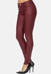 Bordeaux faux leren skinny broek met een hoge tailleband, voorzien van zakken aan de voorkant en een soepele textuur, gedragen met zwarte hakken.