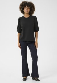 Svart kortärmad topp med puffärmar, kombinerad med mörkblå utsvängda jeans. Mjukt tyg med enkel design, inga synliga mönster.