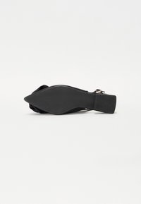 Zapato plano negro con punta afilada, parte superior de tela suave y tacón bajo cuadrado. La suela es lisa con una superficie texturizada. Sin herrajes visibles.