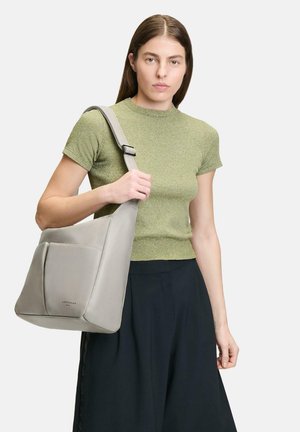 Bolso de hombro de piel gris con una textura suave, que presenta un bolsillo frontal y una correa ajustable, llevado sobre una blusa verde.