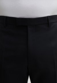 Op maat gemaakte donkerblauwe broek, gemaakt van een gladde stof, met een rechte voorkant, twee riemlussen en subtiele plooidetails.