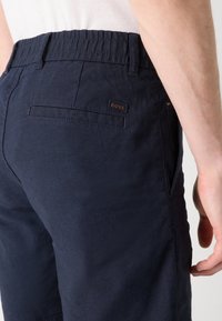 Calções azul-marinho com cintura elástica. Apresentam um bolso traseiro e um pequeno patch de couro com o logotipo. O material parece leve e texturado.